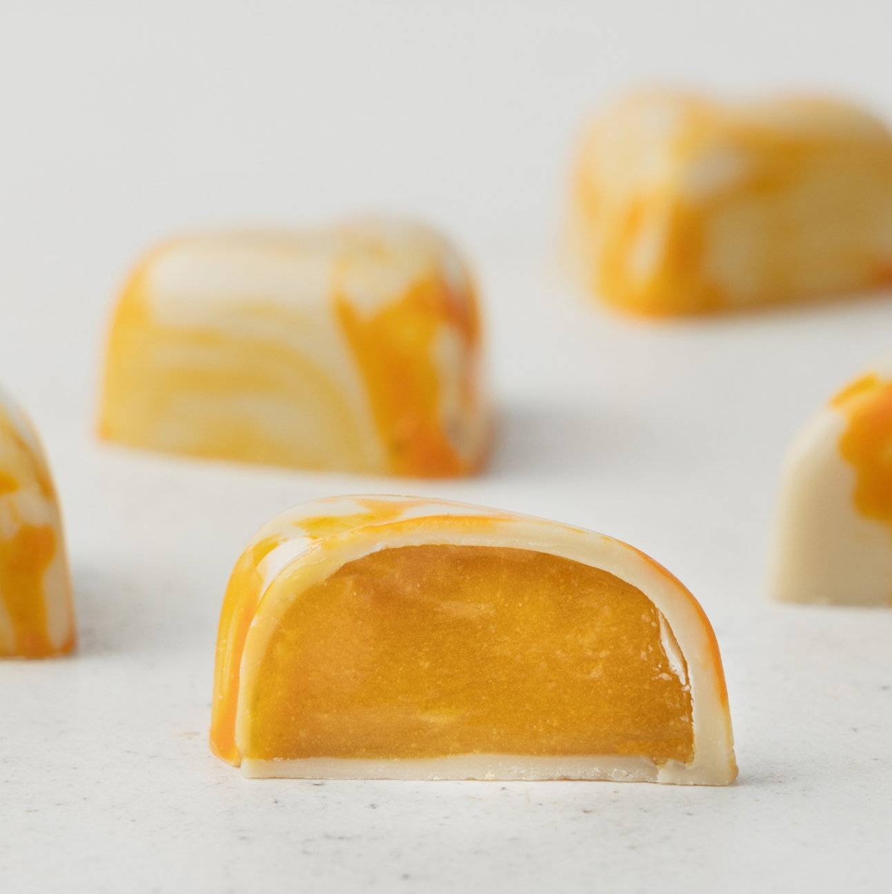 Pohľad zboku na pralinky príchute Mango marakuja uložené symetricky vedľa seba pričom predná pralinka v strede je prekrojená na polovicu. Pralinku Mango marakuja tvorí biela čokoláda na povrchu melírovenej žltej farby, plnená mangovým a marakujovým pyré. Pralinka má tvar srdca.